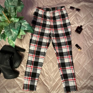 Rutig byxa i svart, vitt och rött - Snygga byxor med ett klassiskt rutigt mönster i svart, vitt och rött. De har en tight passform och är perfekta för att ge en trendig touch till din outfit. Byxorna har en elastisk midja för extra komfort.