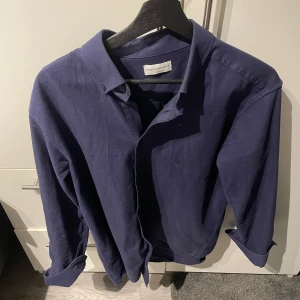 Mörkblå skjorta från These Glory Days - Snygg mörkblå skjorta/overshirt från These Glory Days med klassisk krage och knappar framtill. Skjortan har långa ärmar och är tillverkad i ett lite tjockare material som ger en bekväm passform. Perfekt för en stilren look. Hör av dig vid frågor och funderingar! 