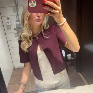 Vinröd kortärmad kofta - Säljer en stilren vinröd kofta med korta ärmar och en knapp framtill. 