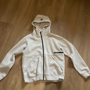 Vit hoodie med dragkedja - Säljer en stilren vit hoodie med dragkedja och huva. Den har en mjuk insida och praktiska fickor framtill. Perfekt för en avslappnad stil. Den är liten i storleken då jag skulle säga att den är mer som XS i storleken 