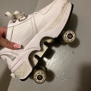 Vita rullskridskor med hjärtan - Snygga vita rullskridskor med perforerade detaljer och hjärtmotiv. Skorna har snörning och fyra hjul för stabil åkning. Perfekta för dig som vill glida fram med stil!