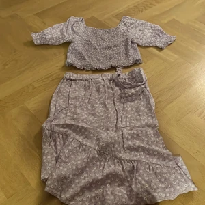 Lila blommig topp+kjol  från Kappahl - Säljer en söt lila blommig topp & kjol  från Kappahl. Toppen har en smockad design och trekvartsärmar. Perfekt för en somrig look! 🌸 Kjolen passar bra till och men kan köpa var och en för sig!!100 för båda