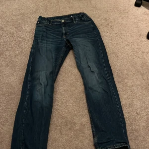 Blå slim fit jeans från H&M - Snygga blå slim fit jeans från H&M med justerbar midja. Perfekta för en stilren look. Klassisk femficksdesign och knappgylf.