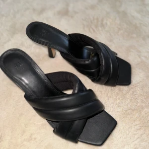 Svarta klackskor med korsade remmar - Stilrena svarta klackskor med korsade remmar och fyrkantig tå. Perfekta för en elegant look. Tillverkade i syntetmaterial med en bekväm passform. 