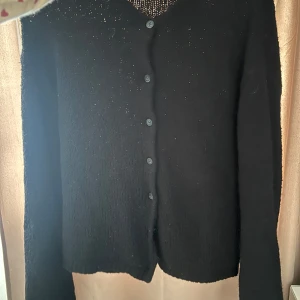 Svart kofta med knappar - Snygg svart kofta med knappar framtill. Perfekt för kyliga dagar och enkel att matcha med olika outfits. Den har långa ärmar och en klassisk design.