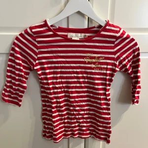 Röd- och vitrandig topp från H&M - Säljer en söt röd- och vitrandig topp från H&M med texten 'Upper East Parker & Co. New York' i guld på bröstet. Toppen har trekvartsärmar och är perfekt för en avslappnad stil. Passar bra till jeans eller kjol för en trendig look.