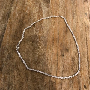 Silverfärgat halsband med tvinnad kedja - Elegant silverfärgat halsband med en fin tvinnad kedja. Perfekt för att lägga till en subtil glans till din outfit. Kedjan har en praktisk karbinhake för enkel användning.