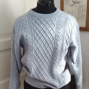 Ljusblå stickad tröja med flätmönster - Säljer en mysig ljusblå stickad tröja med ett snyggt flätmönster. Tröjan har långa ärmar och en rund halsringning. Perfekt för kyliga dagar!