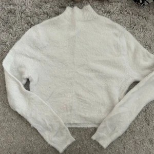 Vit fluffig tröja - Säljer en supermjuk och fluffig vit tröja med hög krage. Perfekt för kyliga dagar när du vill känna dig både stilren och bekväm. Tröjan har långa ärmar och en mysig känsla. Passar perfekt till jeans eller kjol för en avslappnad look.