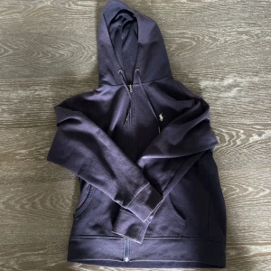 Mörkblå hoodie från Ralph Lauren - Säljer en snygg mörkblå hoodie från Ralph Lauren med dragkedja och det klassiska logotypen på bröstet. Perfekt för en avslappnad stil. Den har långa ärmar och en praktisk huva med dragsko.