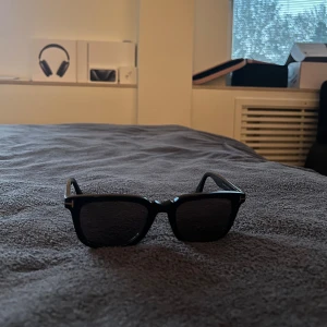 Svarta solglasögon från Tom Ford - Snygga svarta solglasögon från Tom Ford med en klassisk rektangulär form. De har en stilren design med märkets logotyp på sidan av bågarna. Perfekta för att ge en touch av elegans till din stil. Vintage design