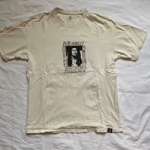Beige Bob Marley t-shirt från Pull&Bear - Säljer en beige t-shirt från Pull&Bear med Bob Marley-tryck. T-shirten har korta ärmar och ett stort tryck av Bob Marley på både fram och baksida. Oversized så passform mot M. 