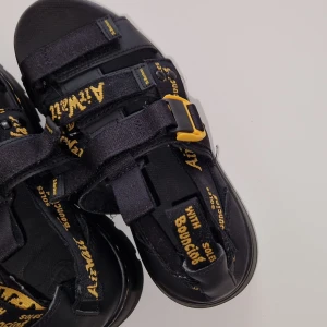 Sandaler från Dr. Martens Person - Svarta sandaler från Dr. Martens med gula detaljer och justerbara remmar med kardborre. Sköna och följsamma. Använda vid ett par tillfällen, riktigt fint skick.