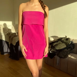 Rosa axelbandslös klänning - Säljer en snygg rosa axelbandslös klänning med en enkel och stilren design. Perfekt för sommarens festligheter. Klänningen har en kort längd och en lös passform som ger en bekväm känsla.