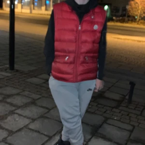 Röd dunväst från Moncler - Snygg röd dunväst från Moncler med dragkedja. Perfekt för lager-på-lager under kyliga dagar. Västen har en klassisk design med Moncler-logga på bröstet.