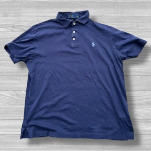 Ralph Lauren piké  - Säljer en klassisk blå pikétröja från Ralph Lauren med broderad logga på bröstet. Tröjan har korta ärmar och knappar vid kragen. Perfekt för en stilren look! 💙