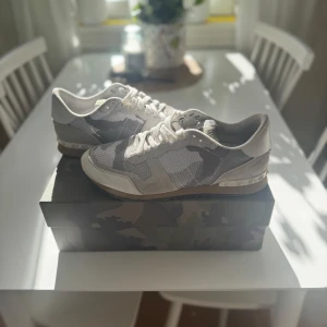 Valentino Garavani sneakers i grått och vitt - Snygga Valentino Garavani sneakers i en stilren grå och vit färgkombination. Skorna har ett diskret kamouflagemönster och är tillverkade i en mix av material som ger en modern look. Perfekta för dig som vill ha något unikt och trendigt. Nypris:4299. Kan även tänkas byta