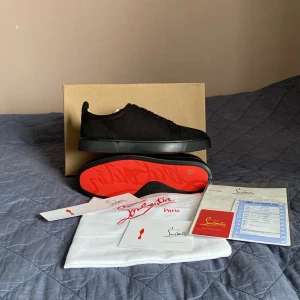 Svarta sneakers från Christian Louboutin - Snygga svarta sneakers från Christian Louboutin med den ikoniska röda sulan. Skorna har en stilren design med snörning och är tillverkade i ett elegant material som ger en lyxig känsla. Perfekta för dig som vill ha en stilren look med en touch av exklusivitet. (A-Cop)