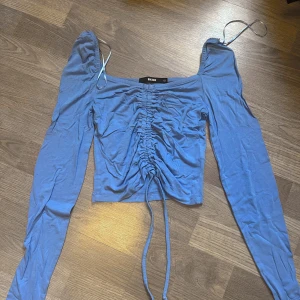 Blå långärmad topp - Snygg blå långärmad topp från Bik Bok med snörning framtill. Den är tillverkad i ett mjukt och elastisk material som känns skönt mot huden.