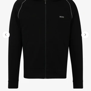 Svart hoodie från BOSS - Snygg svart hoodie från BOSS med dragkedja och diskret logga på bröstet. Tröjan har långa ärmar och en bekväm passform. Perfekt för en stilren look. 