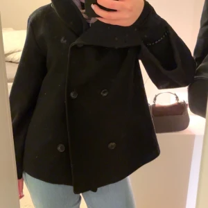 Svart skepparkavaj - Snygg svart skepparkavaj med dubbelknäppning och klassisk krage. Perfekt för en stilren look. Passar bra till jeans eller mer uppklädda outfits. Köpt för 900kr och passar storlek S!!