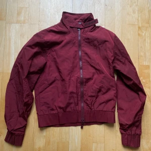 Han Kjøbenhavn Track Jacket XS - Säljer en vinröd jacka från Han Kjøbenhavn. Jackan har en dragkedja framtill och en hög krage med broderad text. Tillverkad i nylon med polyesterfoder, cropped fit. Skickas från Berlin, frakt tillkommer :)