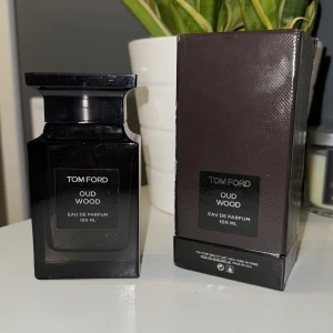 Tom Ford Oud Wood Eau de Parfum 100 ml - Säljer en elegant och lyxig parfym från Tom Ford, Oud Wood Eau de Parfum i en stilren svart flaska på 100 ml. Doften är känd för sina rika och träiga noter, perfekt för den som vill ha en sofistikerad och unik doftupplevelse. 95 ml kvar av den.  OBS KOM MED BUD!