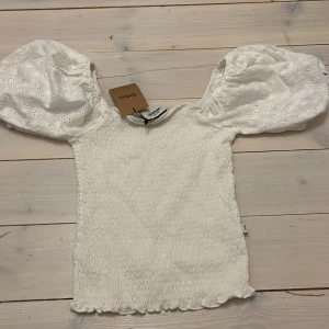 Vit topp med puffärmar från Dobber - Säljer en söt vit topp från Dobber med puffiga kortärmar och ett ribbat material. Perfekt för en somrig look, köpt från Sellpy och aldrig använd! 
