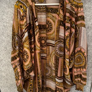 Mönstrad blus från Costa Mani - Säljer en färgglad blus från Costa Mani med ett unikt mönster i rosa, gult och brunt. Blusen har långa ärmar och en lös passform, perfekt för att ge en bohemisk touch till din outfit.