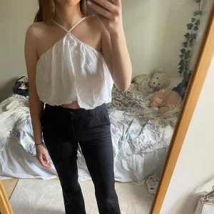 Vit ärmlös halterneck-topp - Säljer en snygg vit halterneck-topp med en luftig och avslappnad passform. Toppen är ärmlös och har en stilren design som passar perfekt för varma dagar. Perfekt att matcha med jeans eller kjol för en trendig look.