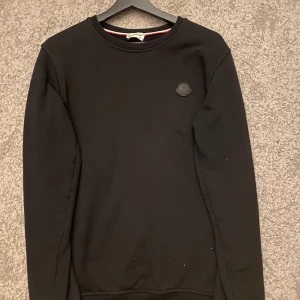 Svart tröja från Moncler - ! TAR GÄRNA BYTEN !Säljer en stilren svart sweatshirt  från Moncler med deras logotyp på bröstet och stort tryck på ryggen. Tröjan har långa ärmar och en klassisk rund halsringning. 