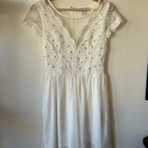 Vit spetsklänning från NLY One - Säljer en vacker vit klänning från NLY One med spetsdetaljer och glittrande stenar. Perfekt för exempelvis studenten.