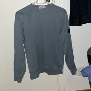 Typ grå blå sweatshirt från Stone Island - Säljer en stilren grå blå sweatshirt från Stone Island. Tröjan har långa ärmar och en klassisk rund halsringning. Perfekt för en avslappnad look. 100% äkta men finns en pytteliten defekt som du kan se på andra bilden. Nypris 1100!