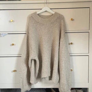 Beige stickad tröja från Gina Tricot - Mysig beige stickad tröja från Gina Tricot med en avslappnad passform. Perfekt för kyliga dagar med sin varma och bekväma design. Tröjan har långa ärmar och en rund halsringning.