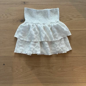 Vit kjol med volanger - Charmig vit kortkjol med volanger och broderade detaljer. Perfekt för en somrig look. Den elastiska midjan ger en bekväm passform.