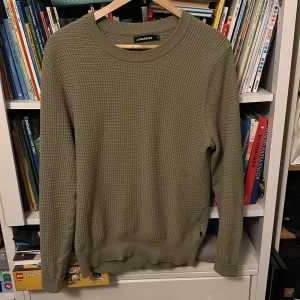 Olivgrön stickad tröja från J.Lindeberg - Säljer en stilren olivgrön stickad tröja från J.Lindeberg. Tröjan har en klassisk rund halsringning och långa ärmar. Perfekt för kyligare dagar och ger en avslappnad men ändå elegant look. Jag är 185 cm lång ish, och denna är ju gränsfall för att vara för liten även om det är en S så den passar definitivt upp mot storlek M. 