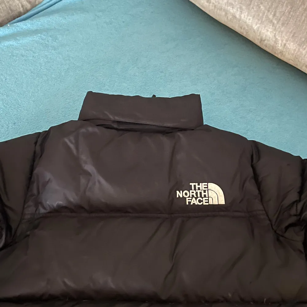 Säljer en svart dunjacka från The North Face med dragkedja och logotyp på bröstet. Jackan har en pufferdesign och är perfekt för kalla dagar. Den är långärmad och har en hög krage för extra värme.. Takit.