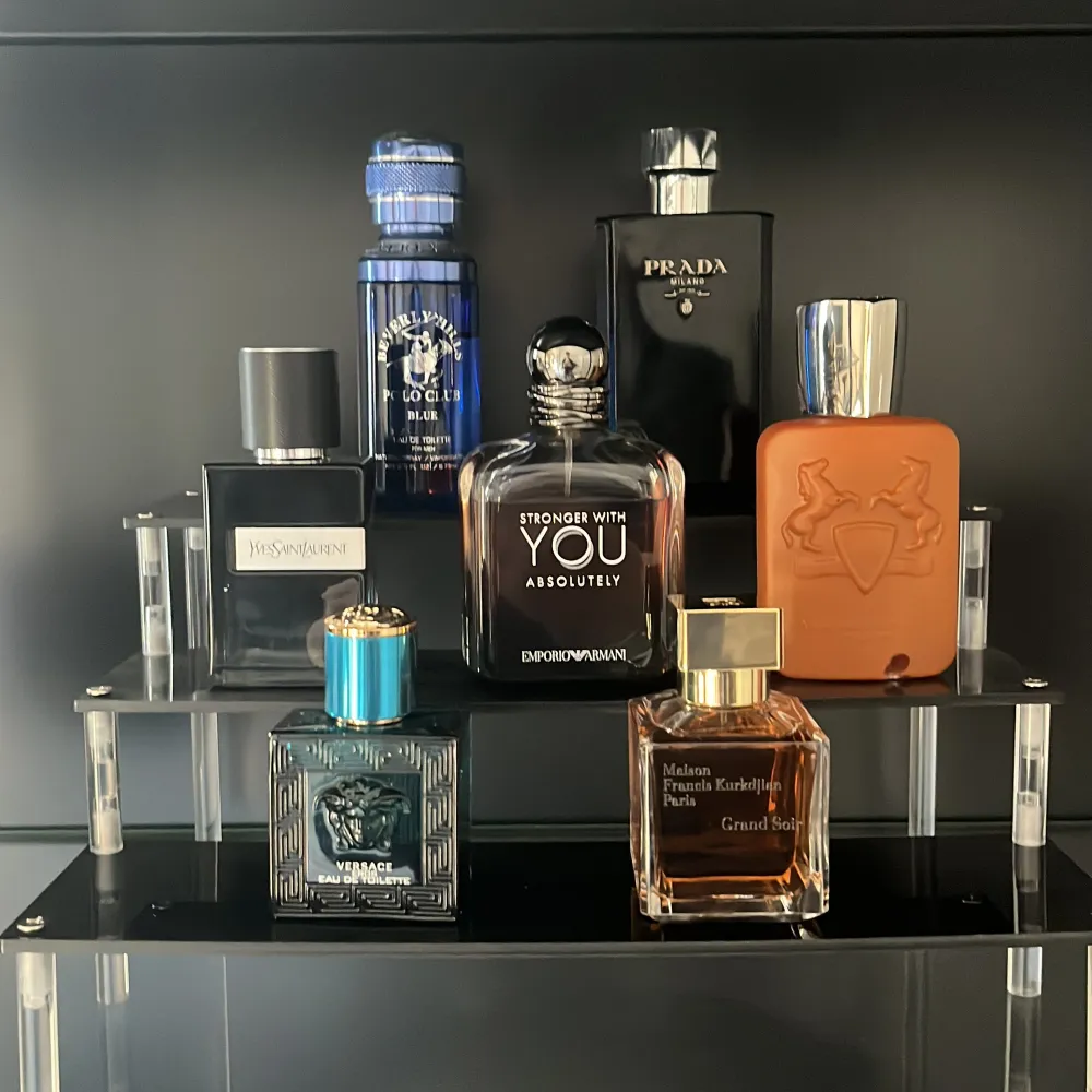 En samling av exklusiva parfymer från kända märken som Emporio Armani, Prada och Versace. Flaskorna har olika former och färger, inklusive svart, blått och orange. Perfekt för den som vill ha en varierad doftgarderob.. Perfume.