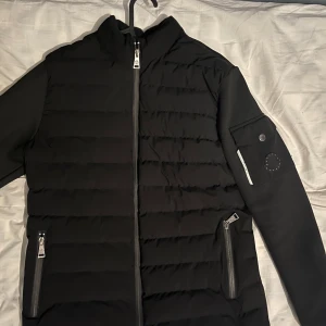 Svart jacka från Moncler - Snygg svart jacka från Moncler med dragkedja och quiltad design. Jackan har långa ärmar och praktiska fickor med dragkedjor. Perfekt för kyligare dagar.