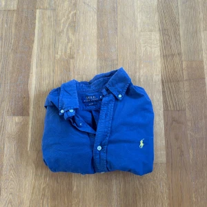 Blå skjorta från Polo Ralph Lauren - Säljer en klassisk blå skjorta från Polo Ralph Lauren med knappar och broderad logga på bröstet. Perfekt för en stilren look. 💙