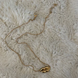 Guldhalsband med läpphänge - Ett oandvänt guldhalsband med ett läppformat hänge. Perfekt för att ge en stilfull touch till din outfit. Kedjan är tunn och smidig med ett justerbart lås för perfekt passform.