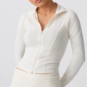 Vit långärmad jacka med dragkedja - Snygg och stilren vit jacka med dragkedja framtill. Den har en tight passform och är perfekt för en sportig look. Jackan är långärmad och tillverkad i ett mjukt och stretchigt material.