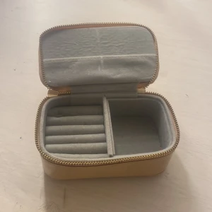 Beige smyckeskrin med dragkedja - Praktiskt beige smyckeskrin med dragkedja och flera fack för förvaring av smycken. Perfekt för att organisera dina favoritsmycken hemma eller på resan.