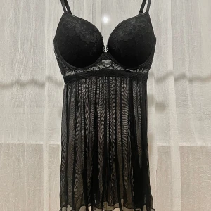 Svart negligé från H&M - Elegant svart negligé från H&M med justerbara axelband och vacker spetsdetalj över bysten. Den har en transparent, flödande kjol som ger en romantisk känsla. STORLEK: EU 40 eller B75 som passar byst 92-95cm.