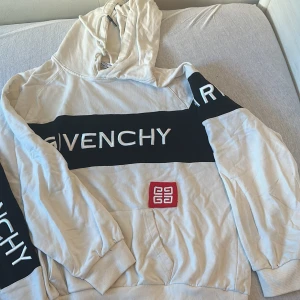 Vit/ svart tracksuit  från Givenchy - Säljer en stilren vit hoodie från Givenchy med svart text och röd logga framtill. Hoodien har en klassisk design med långa ärmar och en bekväm huva med snörning. Perfekt för en avslappnad look.