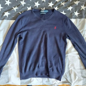 Mörkblå tröja från Polo Ralph Lauren M - Säljer en stilren mörkblå tröja från Polo Ralph Lauren i 100% pima bomull. Tröjan har en v-ringning och ett rött broderat märke på bröstet. Perfekt för en klassisk look. Skick 7/10.