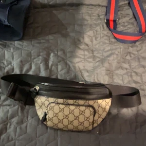  magväska från Gucci - Säljer en snygg magväska från Gucci med det klassiska GG-mönstret. Väskan har en justerbar rem och en dragkedja för säker förvaring. Perfekt för att bära med sig det viktigaste på ett stilfullt sätt.    !!!!! Pris går att diskutera vid snabb affär 
