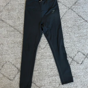 Gråa leggings från Gymshark - Snygga gråa leggings från Gymshark med medel midja. Perfekta för träning med en tight passform som ger bra stöd. Diskret logga på benet och tillverkade i ett stretchigt material för maximal komfort. De är endast testade och är i storlek S. Nypris ligger på 300kr