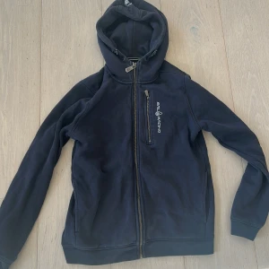 Mörkblå hoodie från Sail Racing - Säljer en mörkblå hoodie från Sail Racing med dragkedja och luva. Storlek 160 men passar även xs/s