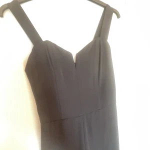 Svart jumpsuit med breda axelband - Elegant svart jumpsuit med breda axelband och en stilren design. Jumpsuiten har en dragkedja bak.